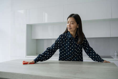 Asian woman cleans and wipes the table with a microfiber cloth in the kitchen. A woman does household chores around the house. The concept of household management.の写真素材