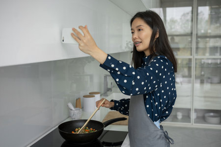 Young Asian woman blogger and online influencer, recording video content about healthy eating, frying vegetables in a frying panの写真素材