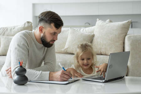 Young father teaches a young daughter using a laptop near the sofa in the living room of the houseの写真素材