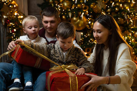 Happy young family with two young sons together open Christmas presents on the background of a...