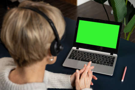 View over the shoulder of a middle-aged woman in a headset, working or studying on a laptop computer...