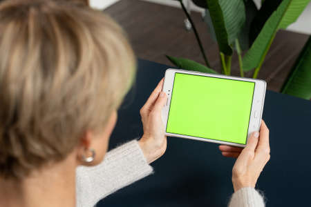 A middle-aged woman is viewing content using a tablet on a green screenの写真素材