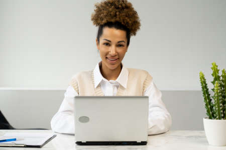 Young African-American female entrepreneur uses a laptop in the workplace and looks at the cameraの写真素材