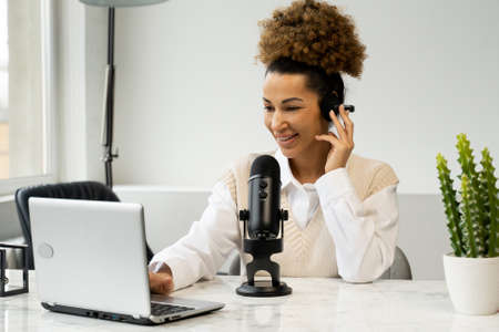 Young black woman is making an online podcast recording for her online show. An attractive African-American business woman speaking into a microphone for a radio program.の写真素材
