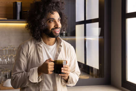 Muslim man enjoys hot tea standing near window in kitchenの写真素材