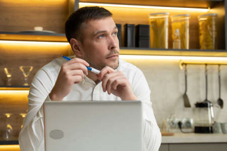 Man watches educational video in laptop turning pen in handsの写真素材