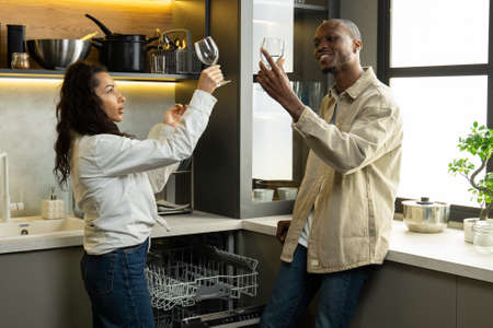 Young couple takes clean glasses out of dishwasher in kitchen