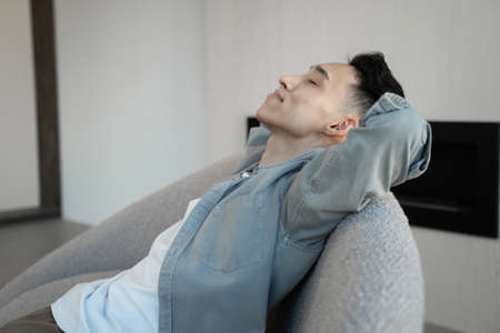 Asian guy leans back on armchair listening to dynamic musicの写真素材