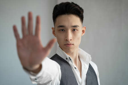 Asian man stretches hand forward making stop gesture