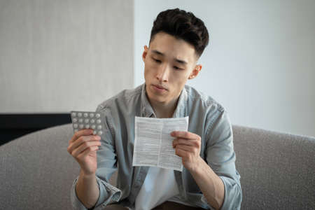 Asian man reads instructions for use of pills for headacheの写真素材