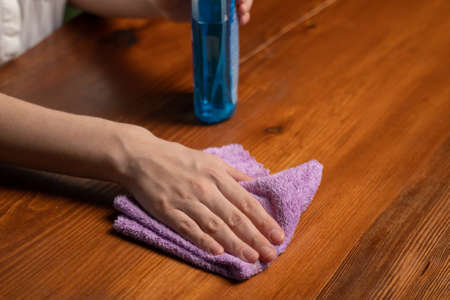 Housewife wipes wooden table in kitchen with duster and detergent. Woman hand cleans table surface....