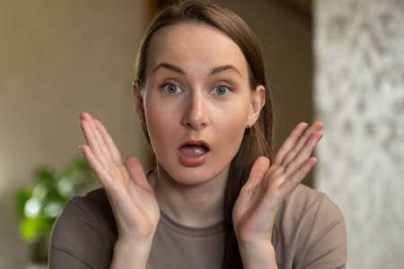 A young pretty woman is surprised with her mouth open, standing with her palms open looking at the...