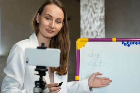 English teacher online at home. Portrait of a woman writing on a blackboard in class.の写真素材