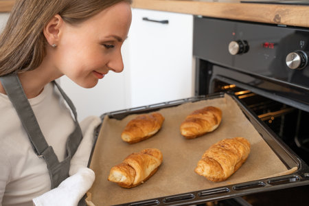 Young woman taking out tray of baked croissants from over in kitchen.の写真素材