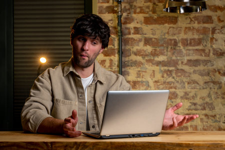 Young black-haired businessman, working with a laptop at a table in the living room of the house, happily surprised.の写真素材