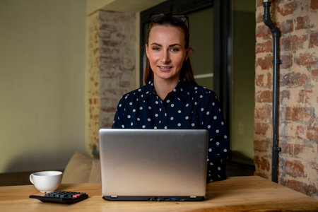 Beautiful woman is working on a laptop computer late at night. A young creative manager feels happy, looks at the camera and smilesの写真素材