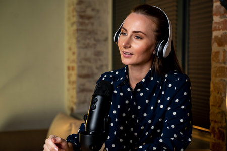Happy woman is recording a podcast with headphones and a microphone, talking and relaxing in her...