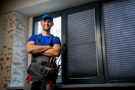Maintenance worker in uniform, blue T-shirt and cap, crossing his arms. A handyman wearing a tool...