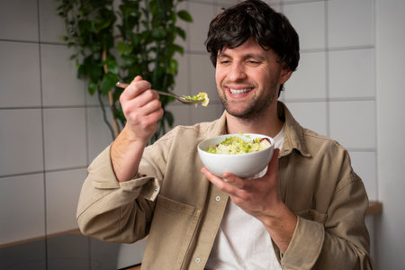 Man in a beige shirt, eating a vegetable salad for lunch, the concept of healthy eating and lifestyle.の写真素材
