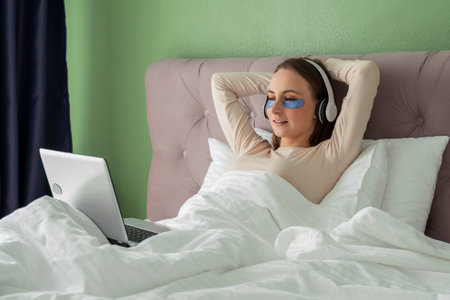 Woman lying in bed listening to music, audiobook, podcast, enjoying meditation for sleep and peace of mind in wireless headphonesの写真素材