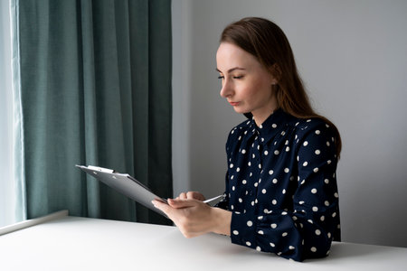 A woman with a pen fills out a form while sitting in the office.の写真素材