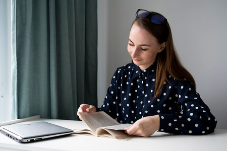 Portrait of a young beautiful woman reading a book, relaxing while working at homeの写真素材