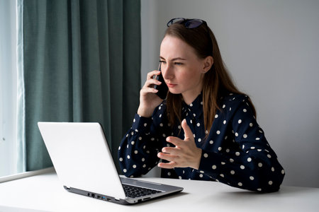 Young businesswoman is a manager working at a laptop and making calls in the office. A professional business lady-manager talks to a client.の写真素材
