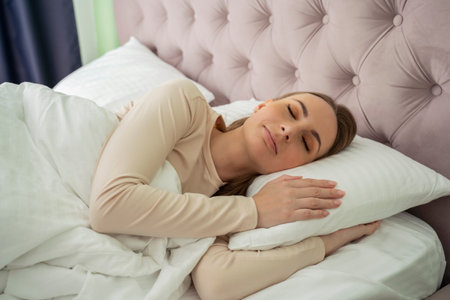 A beautiful attractive woman sleeps and has a sweet dream, lying on a bed in a cozy bedroom and feeling so relaxed and comfortableの写真素材