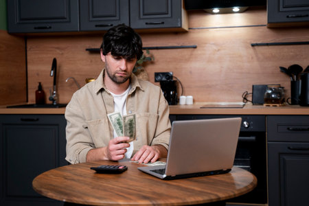 A frustrated man is sitting at a table with utility bills in his hands. A man emotionally reacts to the increased costs of heating, gas and electricity using a calculator.の写真素材