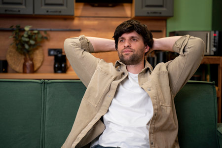 A smiling young man resting at home on the couch with his eyes closed and his hands behind his headの写真素材