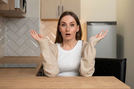 The woman in the kitchen is scared and folded with an expression of surprise, fear and an excited faceの写真素材