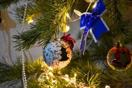 decoration ball with fir-tree ornament and bow on the branch of christmas tree among lights of garlandの写真素材