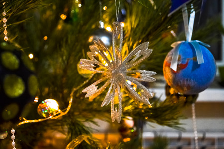 Christmas tree toy on the branch of fir-tree amongst lights of garlandの写真素材