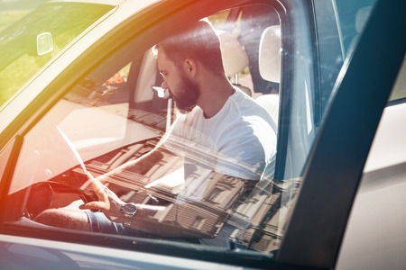 The man behind the wheel starts a white car, casual wear, metal wristwatches, pensive look.の写真素材