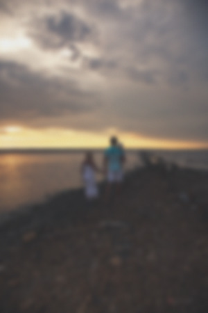 Blurred - young family father mother and daughter at sunset on the lake. Very emotional moment.の写真素材