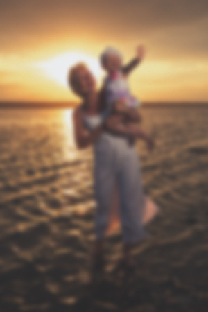 Blurred - Young mother and her daughter at sunset on the lake. Very emotional moment.の写真素材