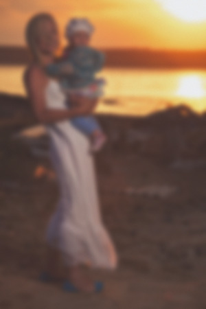 Blurred - Young mother and her daughter at sunset on the lake. Very emotional moment.の写真素材