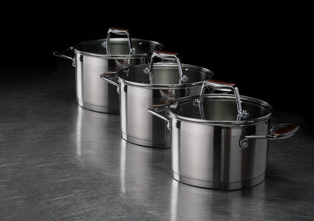 Three metal saucepans with bronze handles on the kitchen steel table.