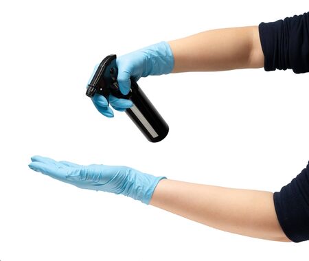 Female hand in a protective rubber medical glove of blue color, holds a black metal bottle of an...