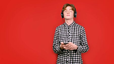 Teenager with red hair in a screeched shirt on a colored background. He closed his eyes while...