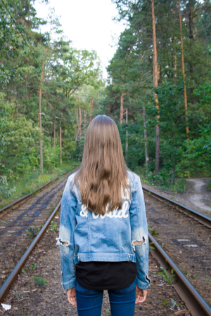 Lonely long haired blond teenage girl in the forest on the railway. Back view