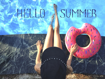 Young woman is relaxing with donut in the swimming pool at spa resort. View from above. Relaxing, vacation, summer holiday idyllic concept. Blue lettering Hello Summer.の写真素材