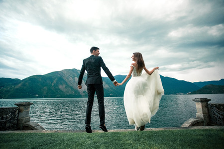 wedding couple running along the grass against the background of the lake and mountainsの写真素材