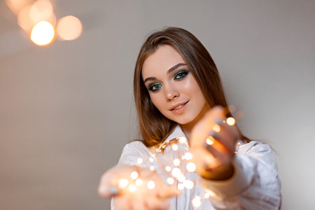 girl in a shirt with a garland on a gray background looks into the frame
