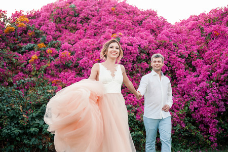 Newlyweds after the wedding in a luxury resort. Romantic bride and groom kiss near pink flowers. Honeymoon. Tropical country.の写真素材