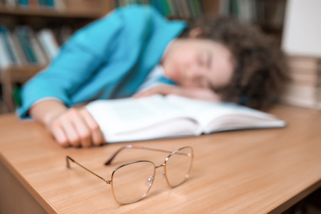 Young beautiful curly girl in glasses and blue suit sitting with books in the library. Student Studyの写真素材