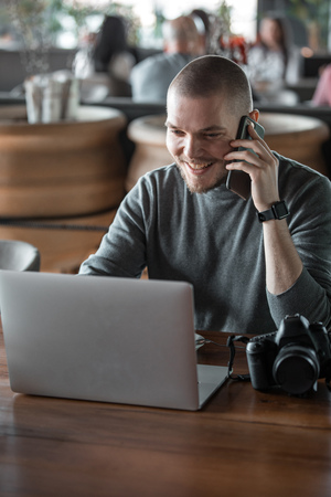 Handsome young photographer with a beard is sitting in cafe with laptop. Photo processingの写真素材
