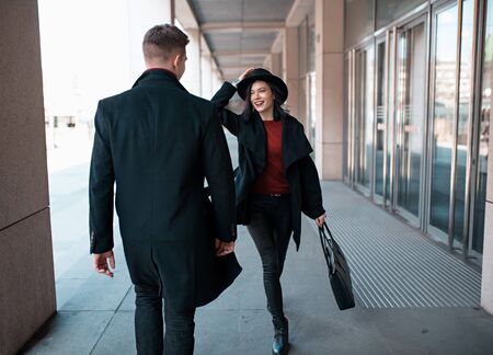 young man in a black coat goes towards a young woman in a black hat and coatの写真素材