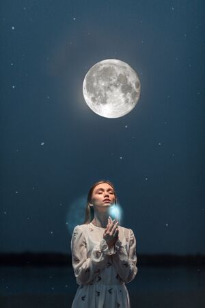 Portrait of a young attractive girl in a long white dress on the beach in moonlight.の写真素材