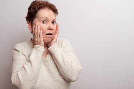 Old woman on a white background in a light sweater. Emotions